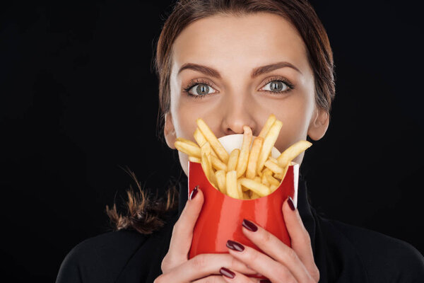 woman covering face with french fries while looking at camera isolated on black