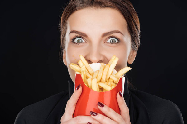 shocked woman covering face with french fries isolated on black