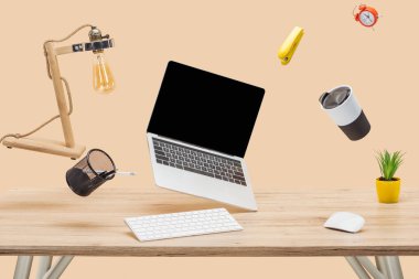laptop with blank screen and stationery levitating in air at workplace isolated on beige clipart