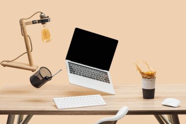 laptop ile boş bir ekran ve bej izole kahve sıçrama ile yukarıda çalışma alanı thermomug ile havada levitating lamba