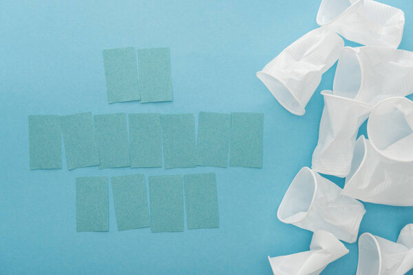 top view of white plastic cups and empty sticky notes with copy space on blue background 