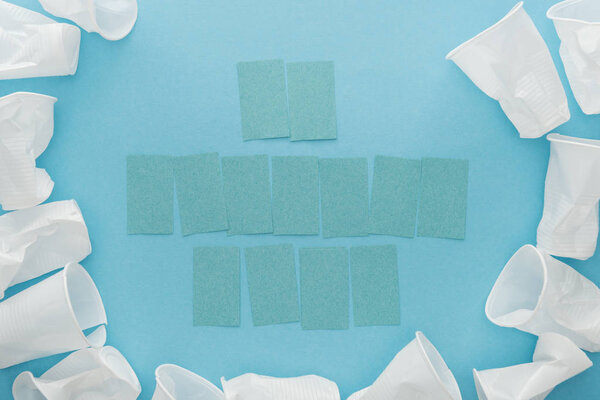 top view of white plastic cups and empty sticky notes with copy space on blue background 