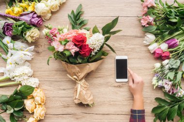 Kısmi Çiçekçi Çiçek ahşap yüzeyde yakınındaki boş ekran ile smartphone kullanarak görünümünü