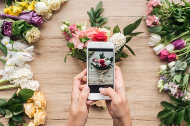 Smartphone ve çiçek buketi alarak fotoğraf ahşap yüzeyde tutan çiçekçi görünümünü kırpılmış