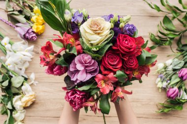 Partial view of florist holding bouquet of fresh flowers on wooden surface clipart