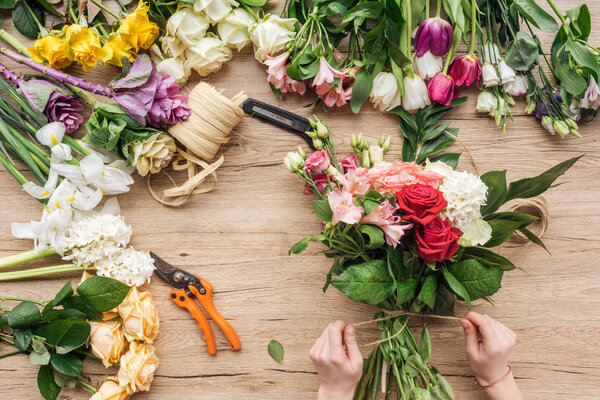 Cropped view of florist making flower bouquet on wooden surface