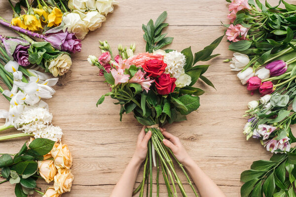 Cropped view of florist holding flower bouquet on wooden table