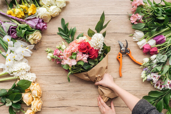 Cropped view of florist making flower bouquet on wooden surface