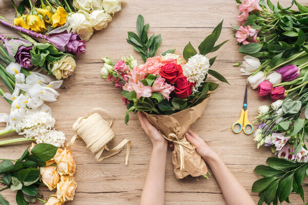 Cropped view of florist making flower bouquet on wooden surface