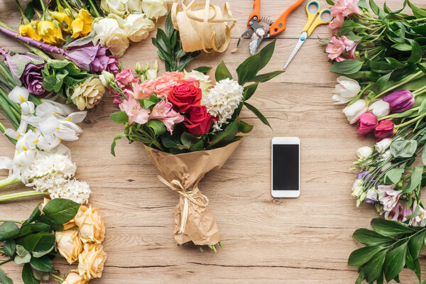 Fresh flowers and smartphone with blank screen on wooden surface