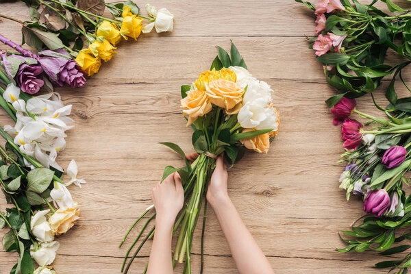 Partial view of florist holding bouquet of fresh flowers on wooden surface