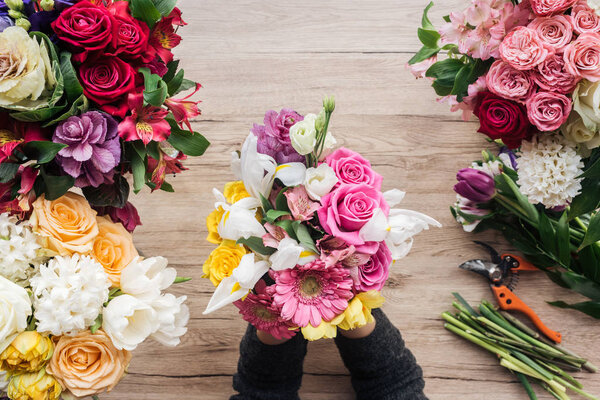 Partial view of florist holding bouquet of fresh flowers on wooden surface