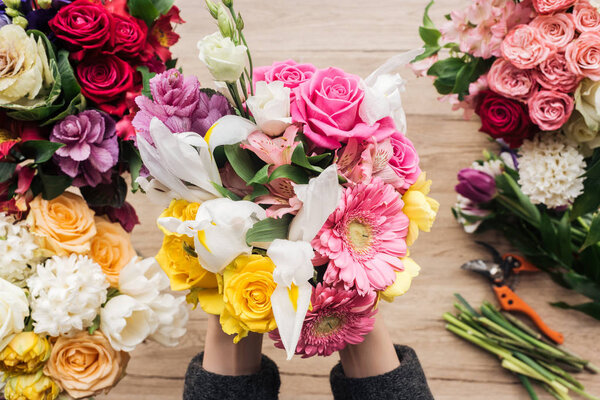 Partial view of florist holding bouquet of fresh flowers on wooden surface