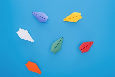 Flat lay with colorful paper planes on blue surface clipart