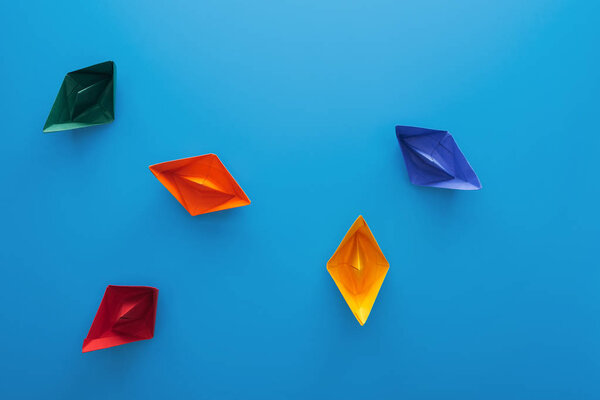 Top view of colorful paper boats on blue surface