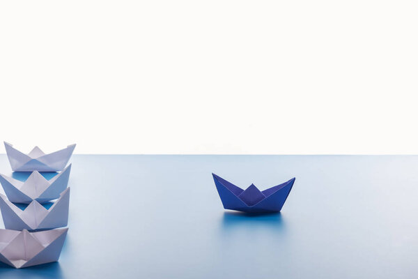 Бумажные лодки на светло-голубой поверхности на белом фоне
