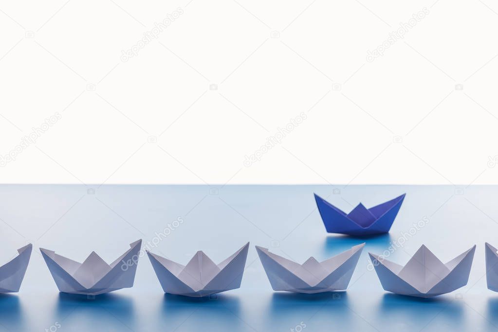 Paper boats on light blue surface on white background