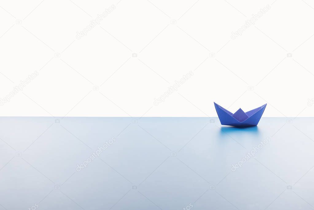 Blue paper boat on light surface on white background