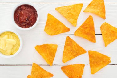 top view of tasty nachos and sauces on white wooden table  clipart