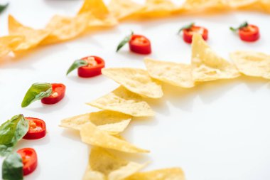 Beyaz arka planda fesleğen ve lezzetli nachos ile Chili Peppers seçici odak 