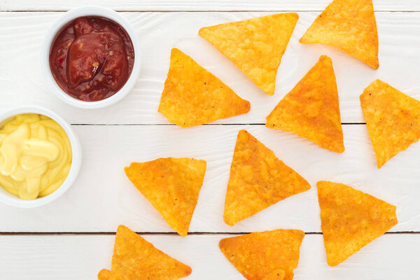 top view of tasty nachos and sauces on white wooden table 