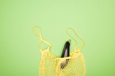top view of ripe eggplant in yellow string bag on light green background clipart