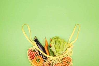 top view of yellow string bag with organic vegetables on light green surface with copy space clipart