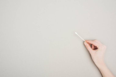 cropped view of woman holding cotton swab on grey background clipart