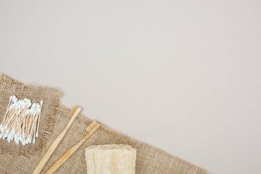 bamboo toothbrushes, organic loofah, cotton swabs and brown sackcloth on grey background clipart