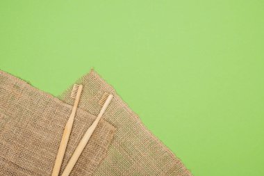 bamboo toothbrushes and brown sackcloth on light green background clipart