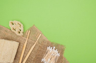 bamboo toothbrushes, organic loofah, cotton swabs and brown sackcloth on light green background clipart