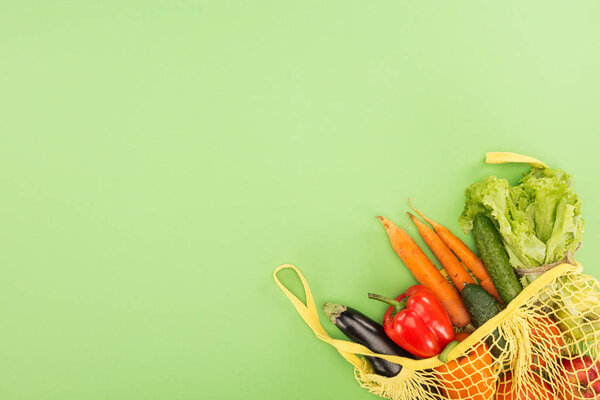 red bell pepper, carrots, lettuce, cucumbers and eggplant in yellow string bag on light green background
