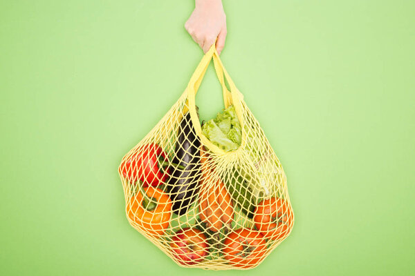 cropped view of woman holding string bag with raw vegetables