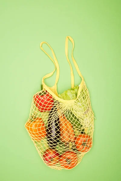 top view of yellow string bag with ripe organic vegetables on light green surface