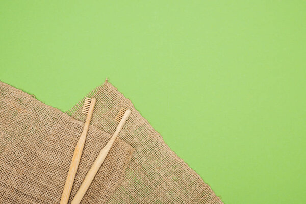 bamboo toothbrushes and brown sackcloth on light green background