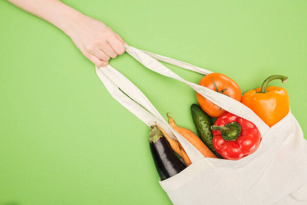 partial view of woman holding handle of cotton bag full of ripe vegetables