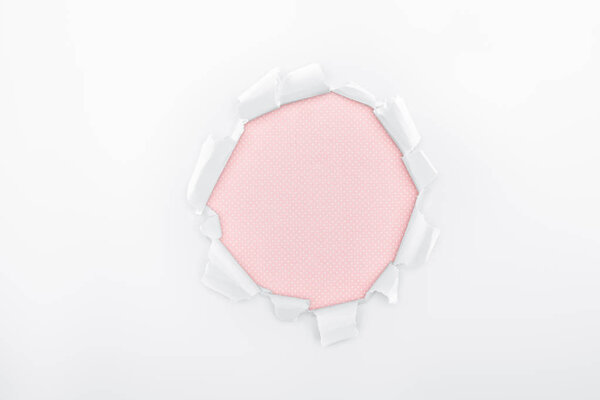 ragged hole in textured white paper on pink background 