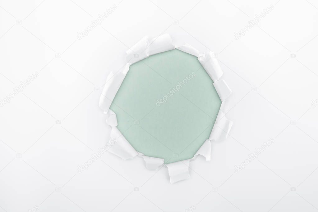 ragged hole in textured white paper on light blue background 