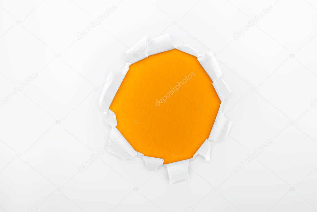 ragged hole in textured white paper on orange background 