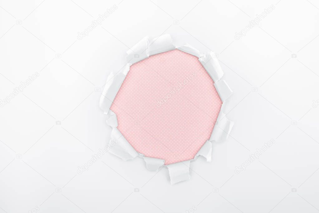 ragged hole in textured white paper on pink background 