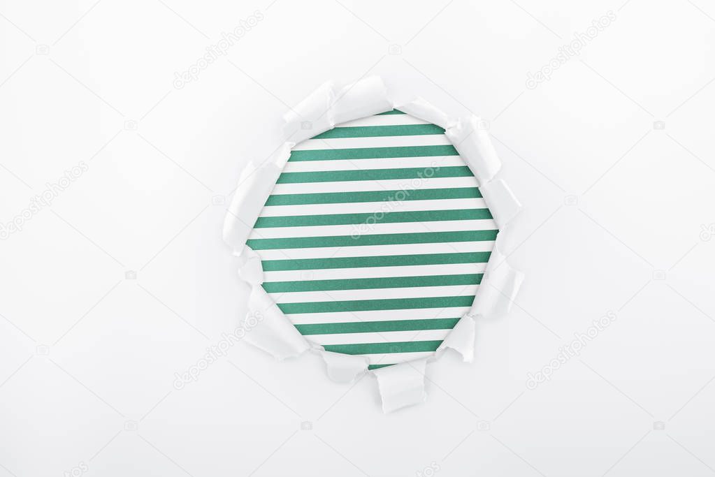 ragged hole in textured white paper on green striped background 