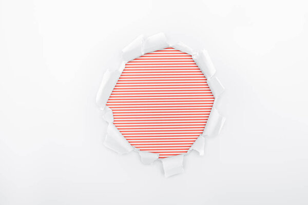 ripped hole in textured white paper on red striped background 