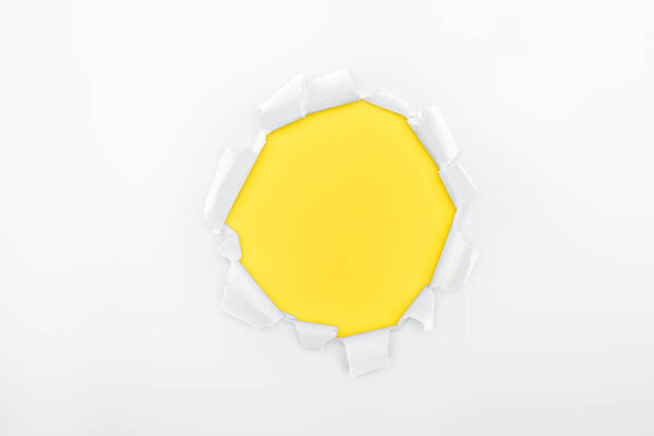 torn hole in white textured paper on yellow background 