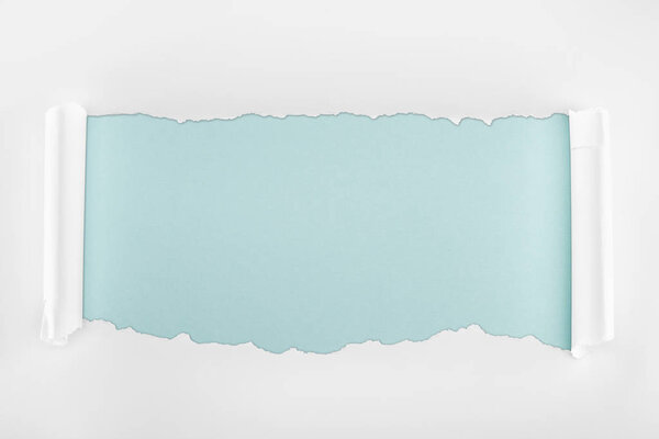 tattered white textured paper with curl edges on light blue background 