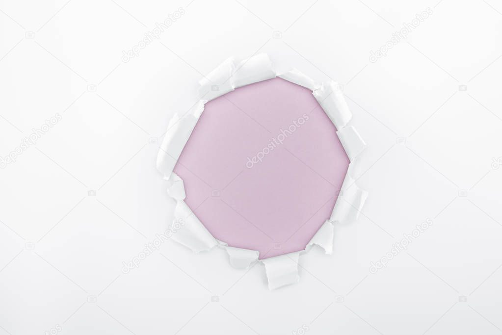 ragged hole in textured white paper on light purple background 