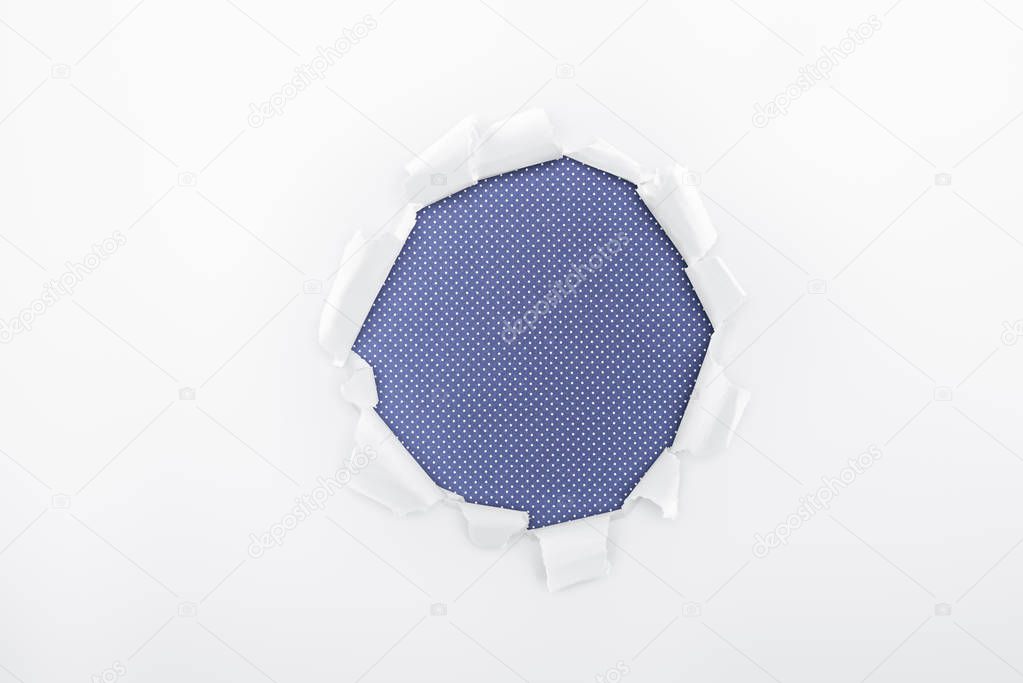 ripped hole in textured white paper on blue dotted background 