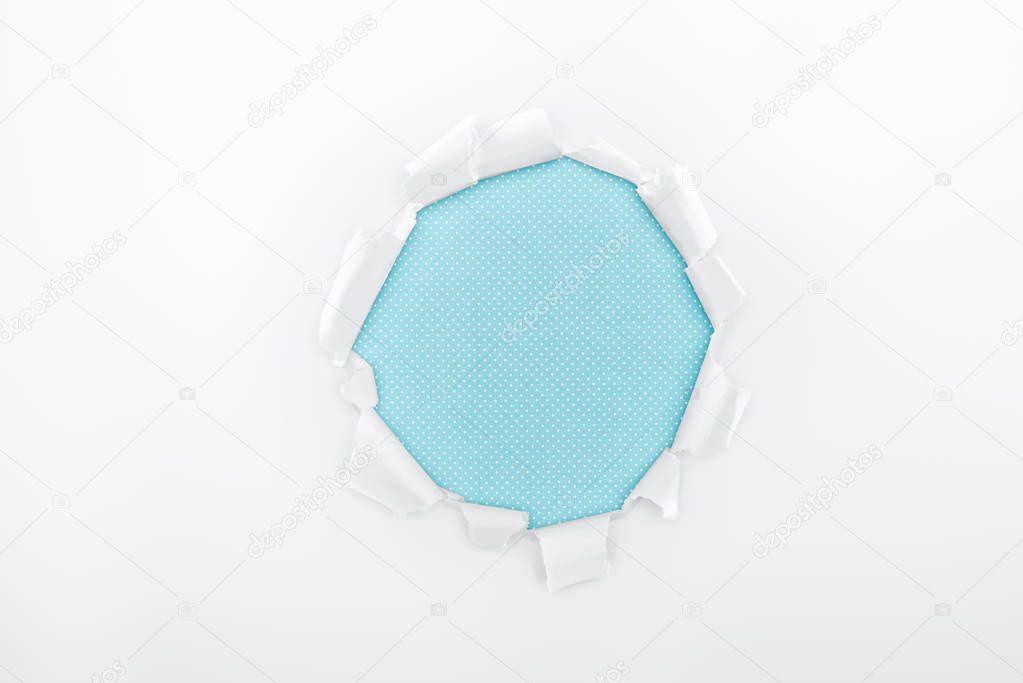 torn hole in textured white paper on light blue background 