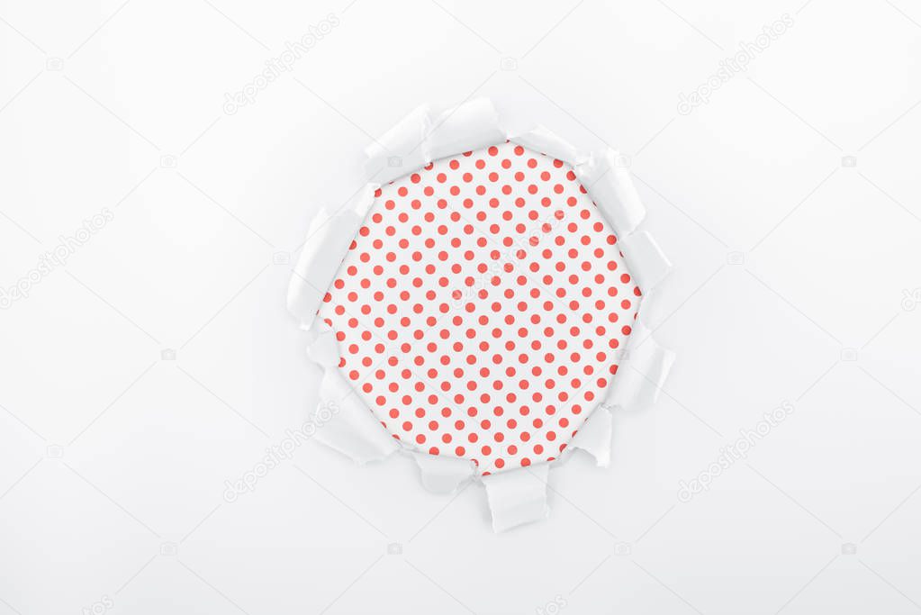 ripped hole in textured white paper on red polka dot background 