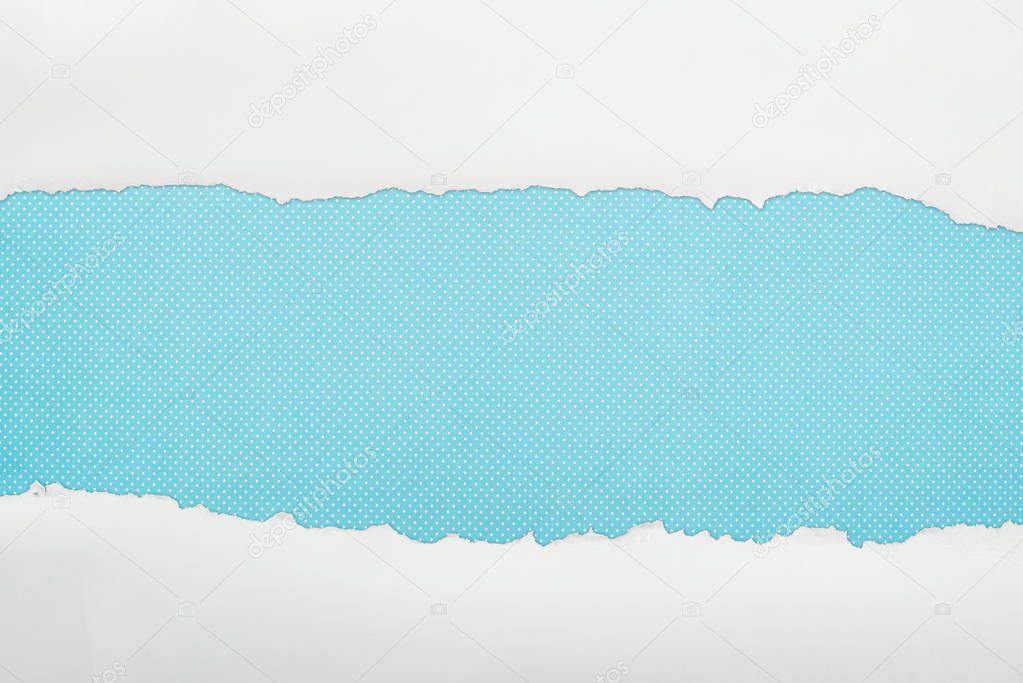 ripped white textured paper with copy space on blue polka dot background 