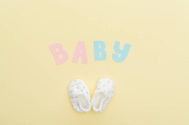 top view of booties and baby lettering isolated on yellow clipart